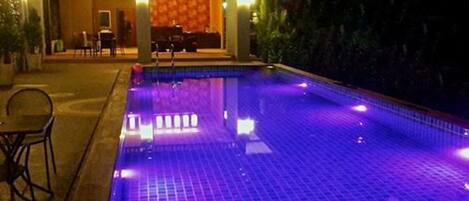 A swimming pool with a tiled floor and a seating area with chairs and tables.