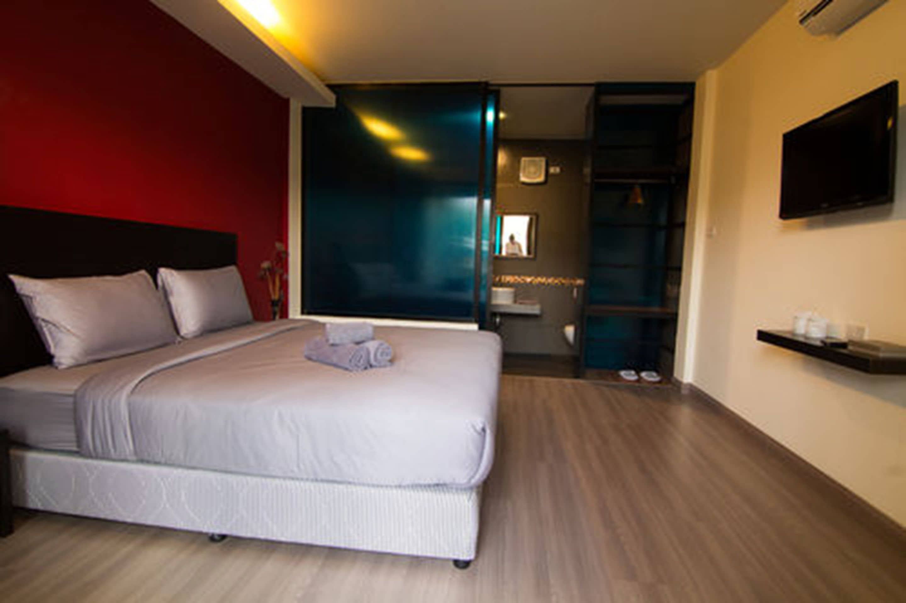 Una habitación de hotel moderna con una cama grande, un televisor montado en la pared y un baño visible a través de una puerta abierta.