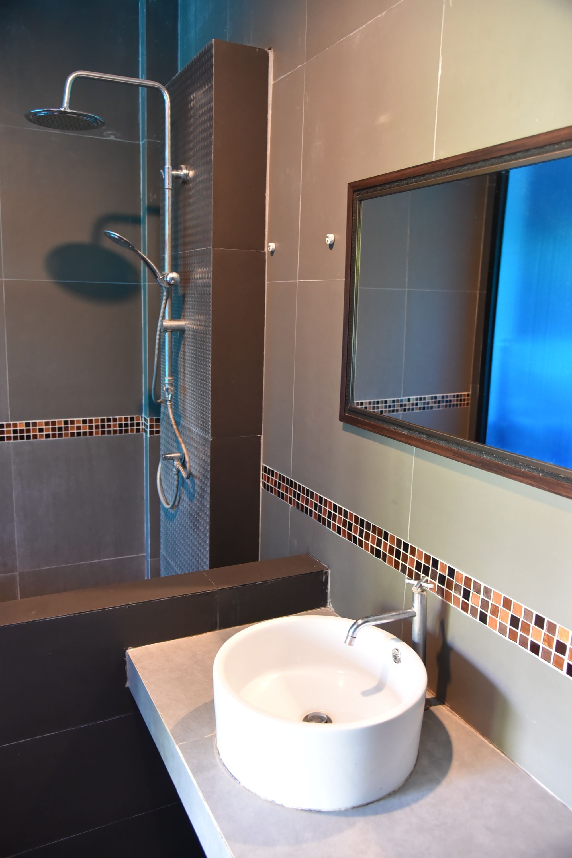 Une salle de bain avec un lavabo blanc, une douche équipée d’un pommeau de douche à main et un miroir au-dessus du lavabo.