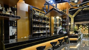 A bar area with a black countertop, shelves of liquor bottles, and black bar stools. - Media Hotel & Residence (Bangkok)