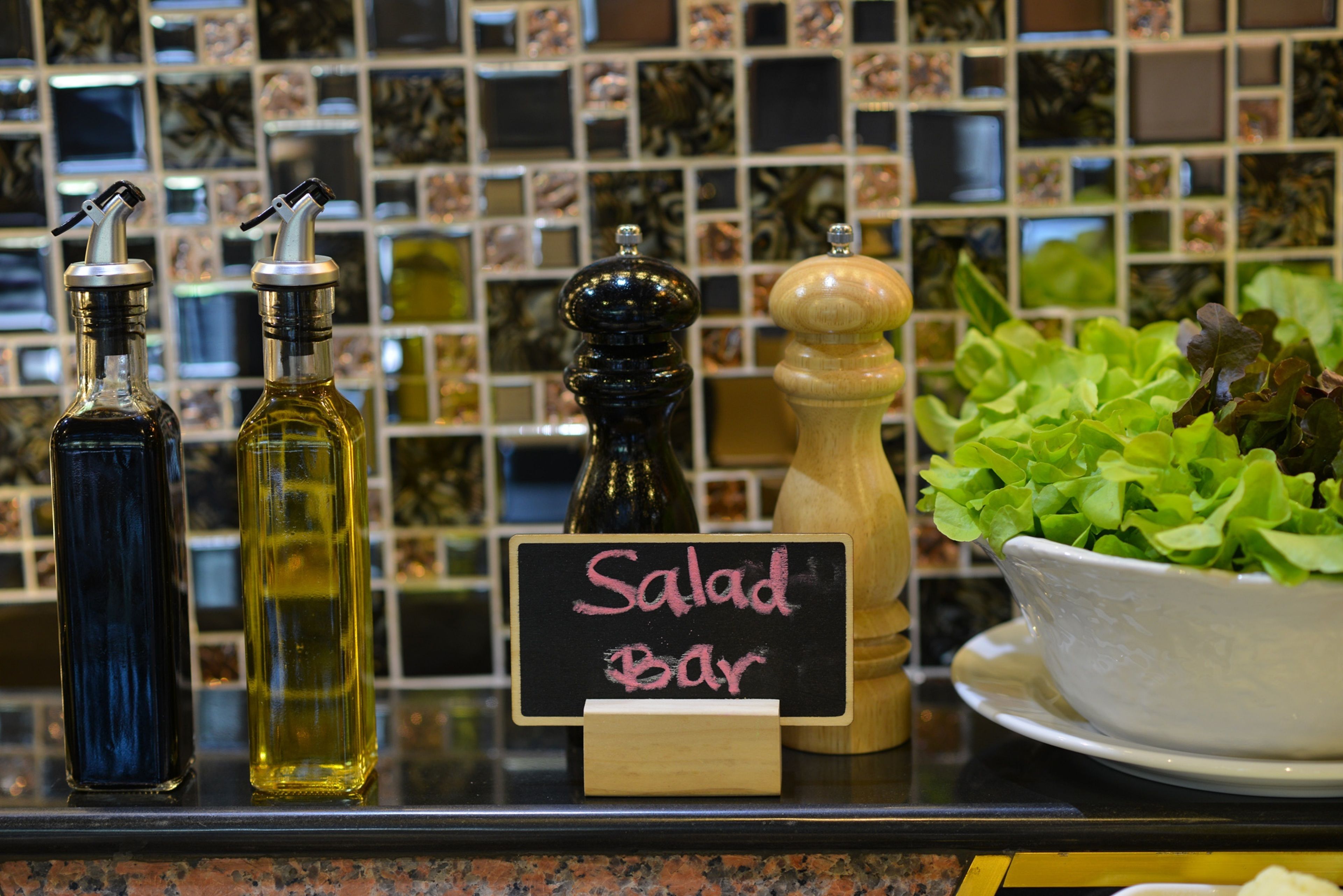 A counter with condiments, a sign reading "Salad Bar", and a bowl of lettuce.