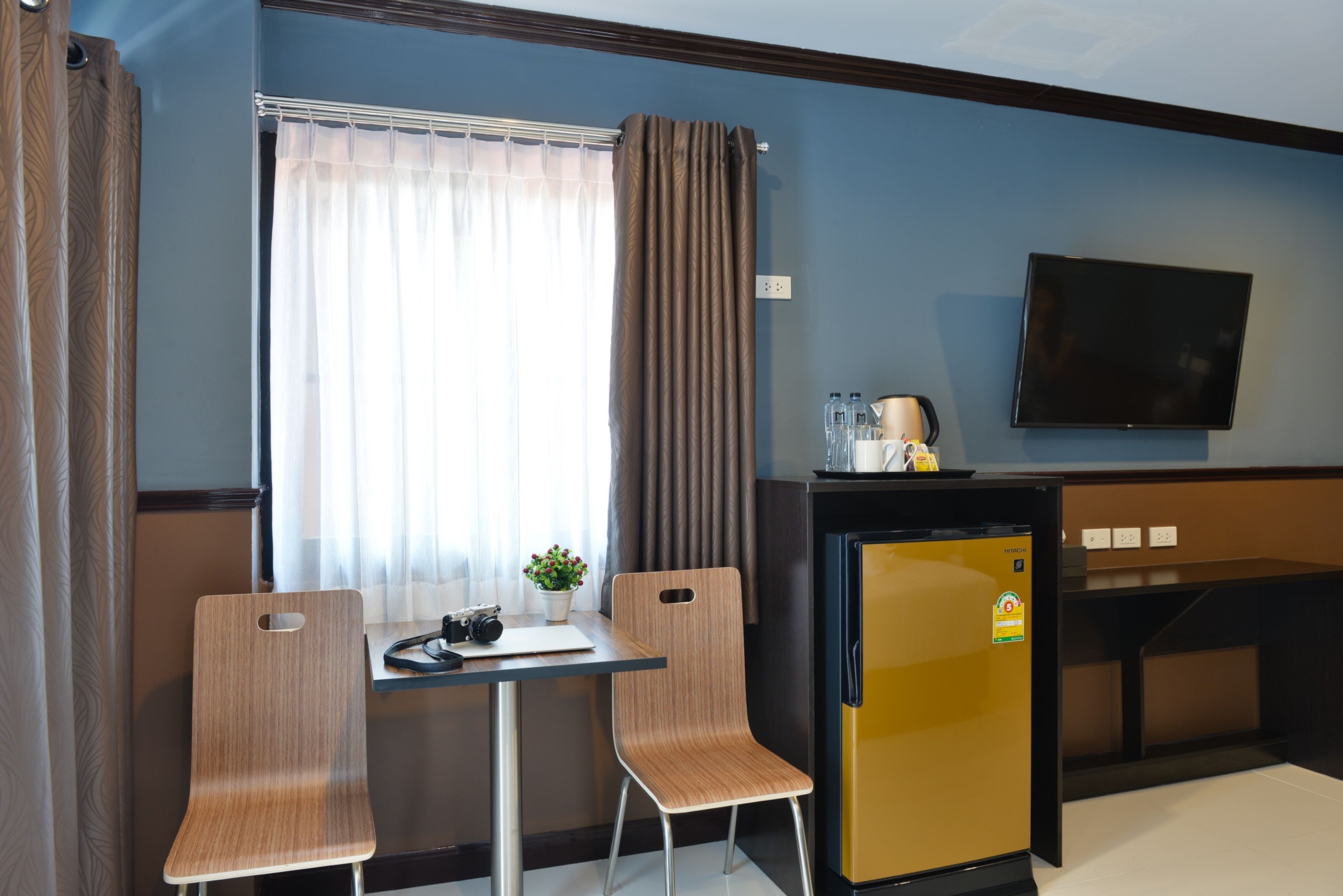 A compact hotel room with a small table, two chairs, a television, a refrigerator, and a window with curtains.