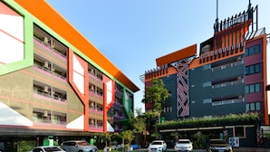 A modern building with multiple floors, balconies, and a parking area with several cars. - Media Hotel & Residence (Bangkok)