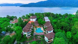 A resort with multiple buildings, a swimming pool, and a view of the sea with boats.