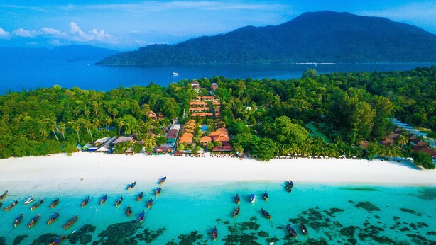 An aerial view of a resort with multiple buildings, a beach, and numerous boats in the water.