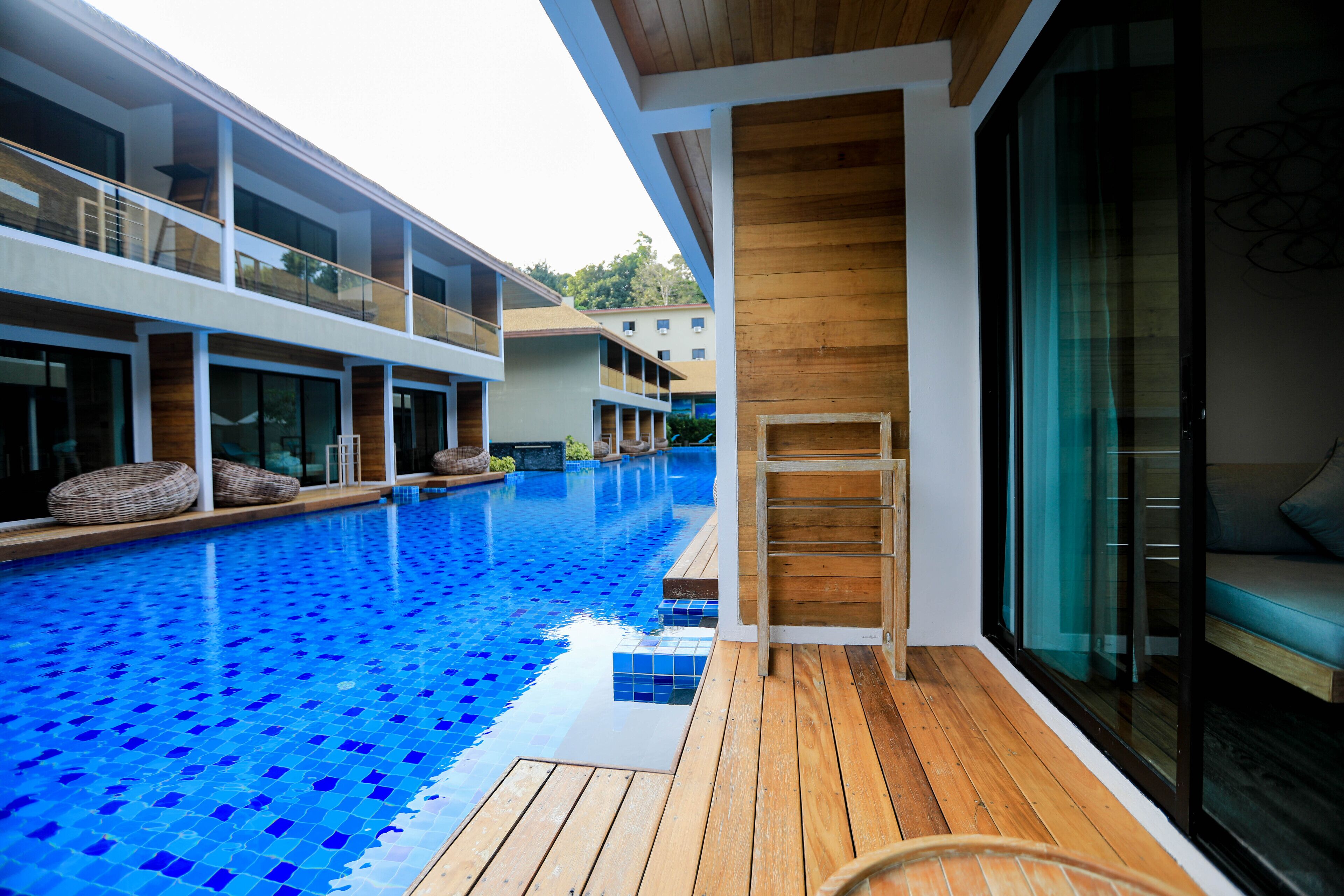 Un hôtel moderne doté d’une piscine, d’une terrasse en bois et de rampes en verre.