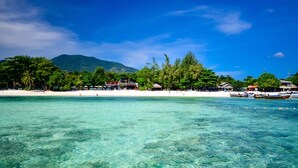 Une plage à l’eau turquoise et limpide, bordée de sable blanc, avec, en arrière-plan, de luxuriantes collines verdoyantes.
