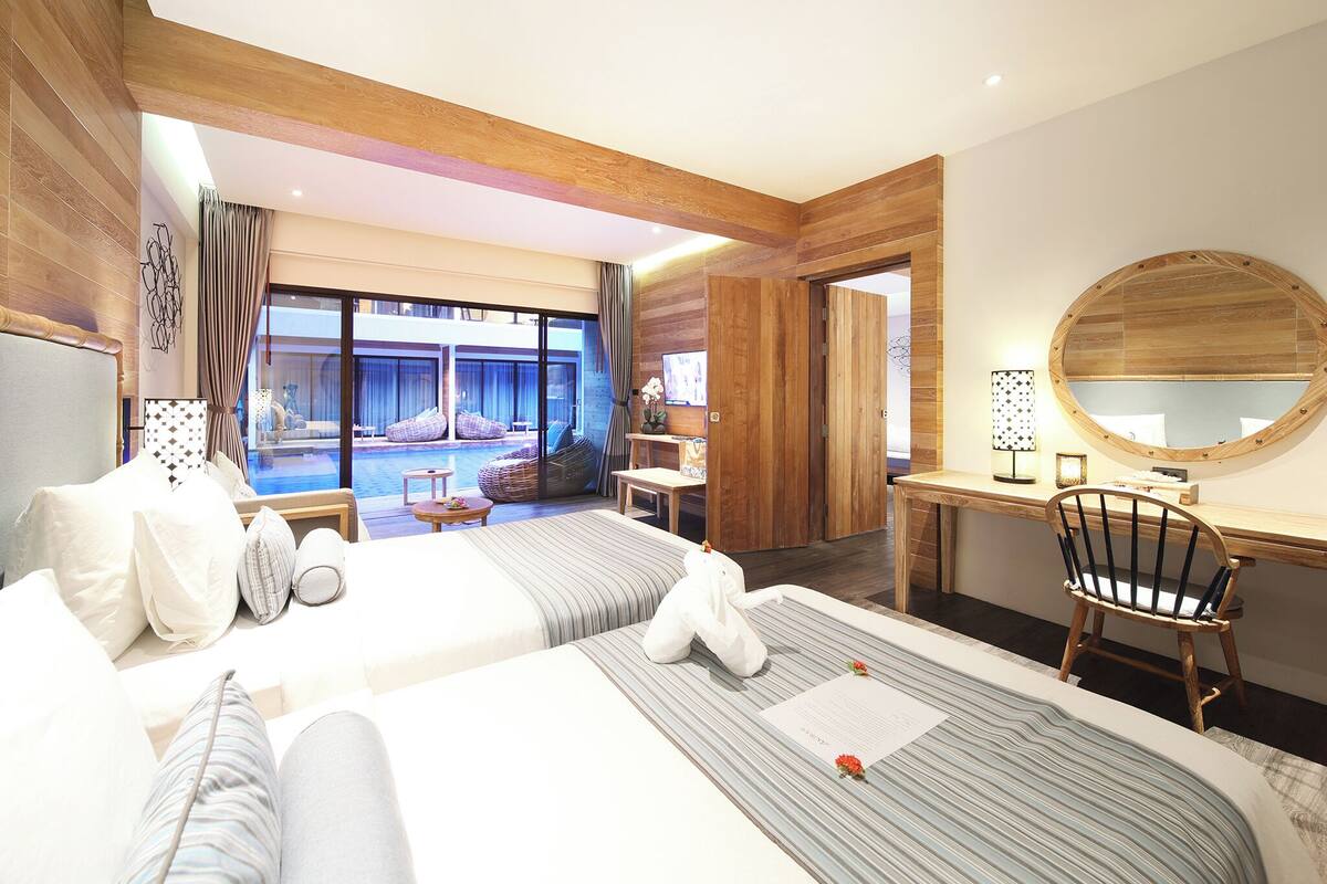 Quarto de hotel com uma cama grande, uma escrivaninha, uma cadeira, um espelho redondo e vista para uma área de piscina ao ar livre.