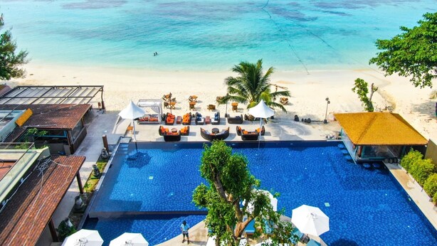 Un espace piscine avec des chaises longues et des parasols, une plage aux eaux turquoise et cristallines, et une vue sur l’océan.