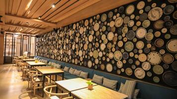 Un restaurante con una barra larga y varias mesas, una pared decorada con numerosas vajillas y un techo de madera.