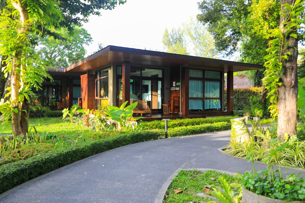 Um edifício moderno com fachada de vidro, cercado por vegetação exuberante e um caminho curvo que leva à entrada.
