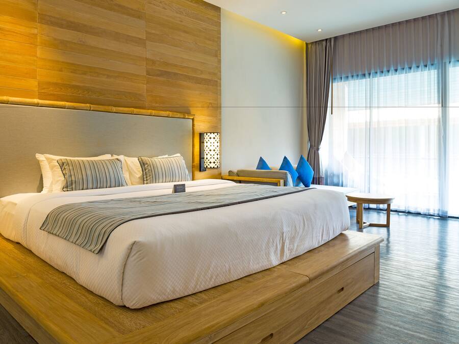 A modern hotel room with a large bed, wooden headboard, and a small seating area.
