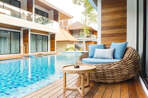 A poolside area with a wicker sofa and a small wooden table.
