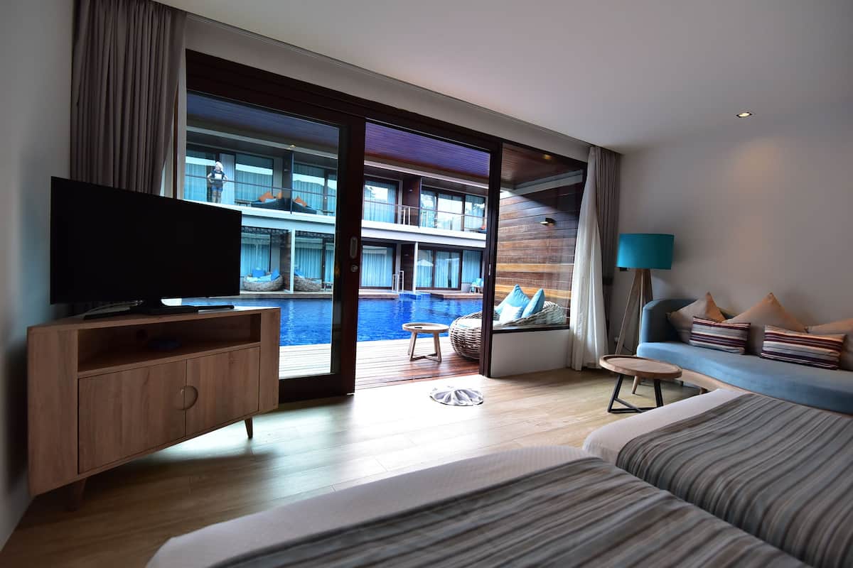 Quarto de hotel moderno com uma cama grande, televisão, cómoda de madeira e vista para a piscina e um edifício.