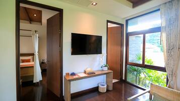 Une chambre d’hôtel avec un plancher en bois, un téléviseur fixé au mur, un bureau avec un panier, et une fenêtre donnant sur un paysage verdoyant.