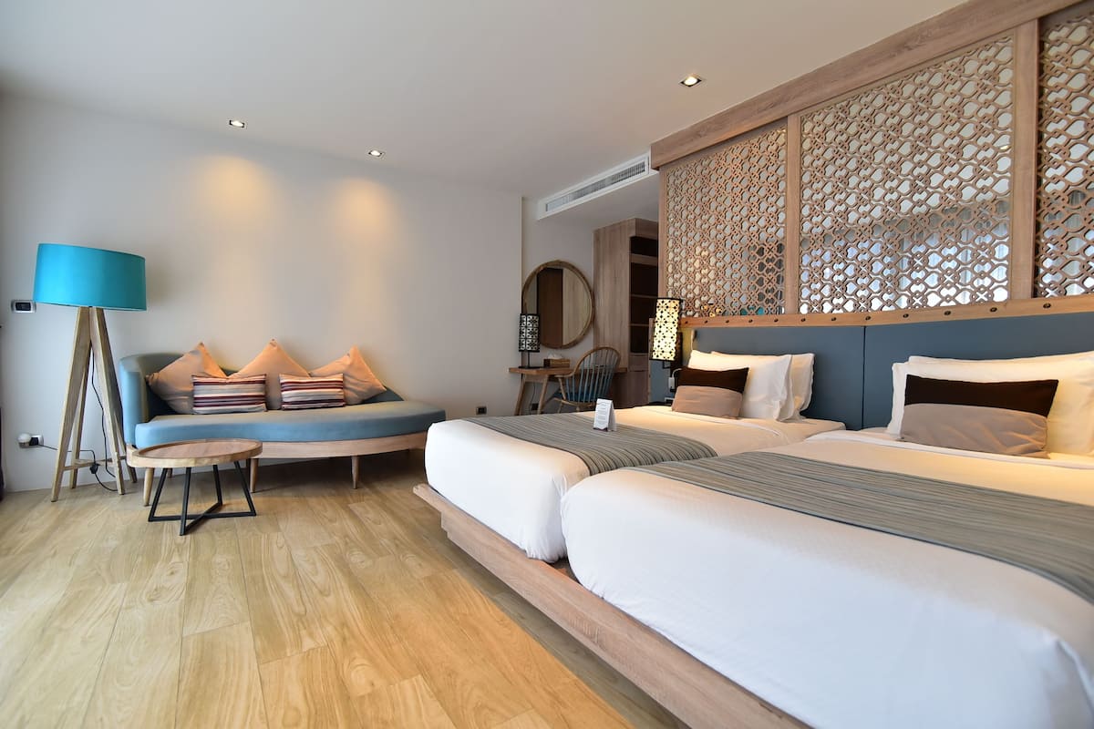 Quarto de hotel moderno com uma cama grande, área de estar com almofadas, uma pequena mesa e um painel decorativo na parede.