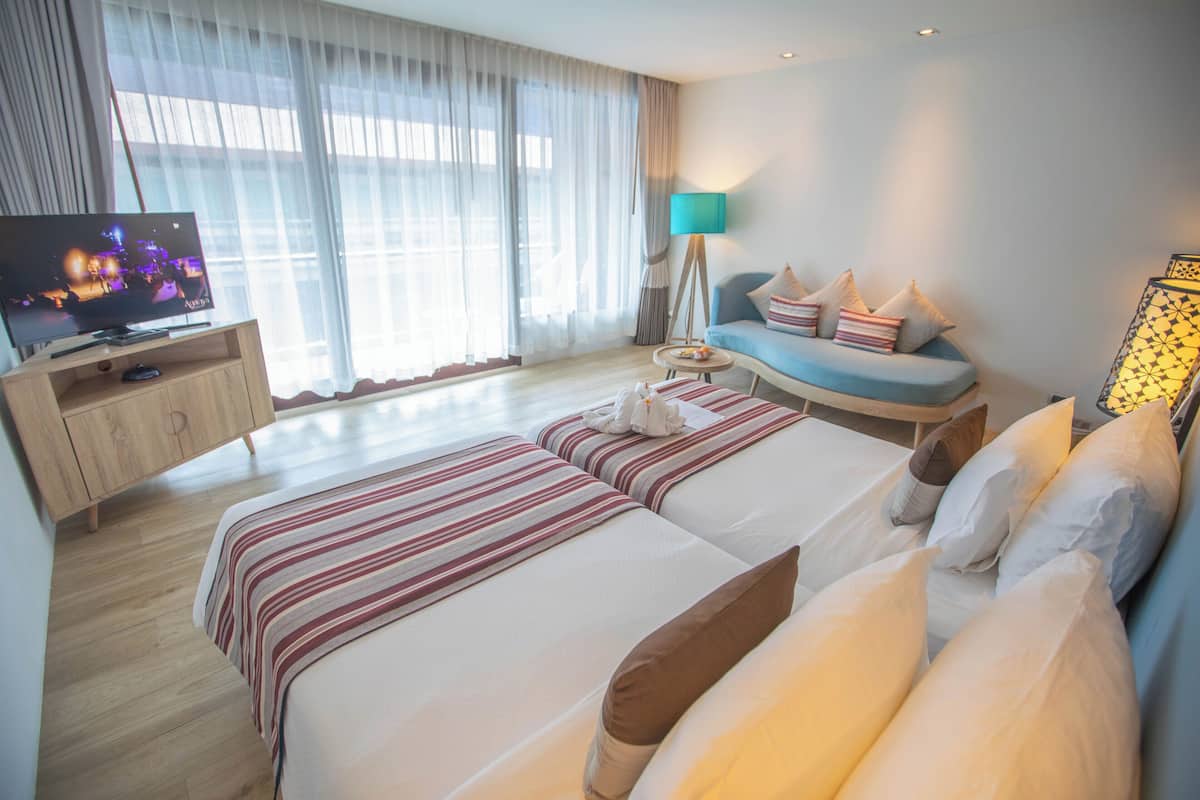 Quarto de hotel com duas camas, televisão, luminária e vista para o exterior.