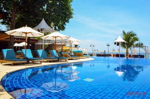 A swimming pool with lounge chairs and umbrellas, surrounded by trees and a clear sky.