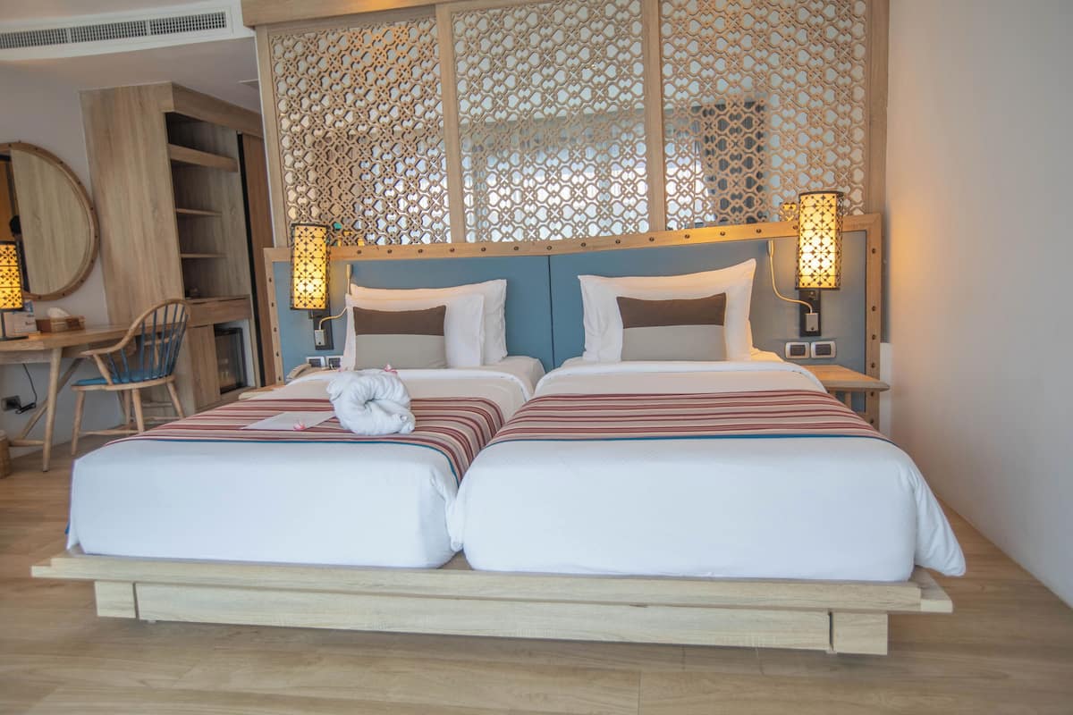 Cama de casal com duas almofadas, mesa de cabeceira, uma cadeira e um biombro decorativo com luminárias fixadas na parede.