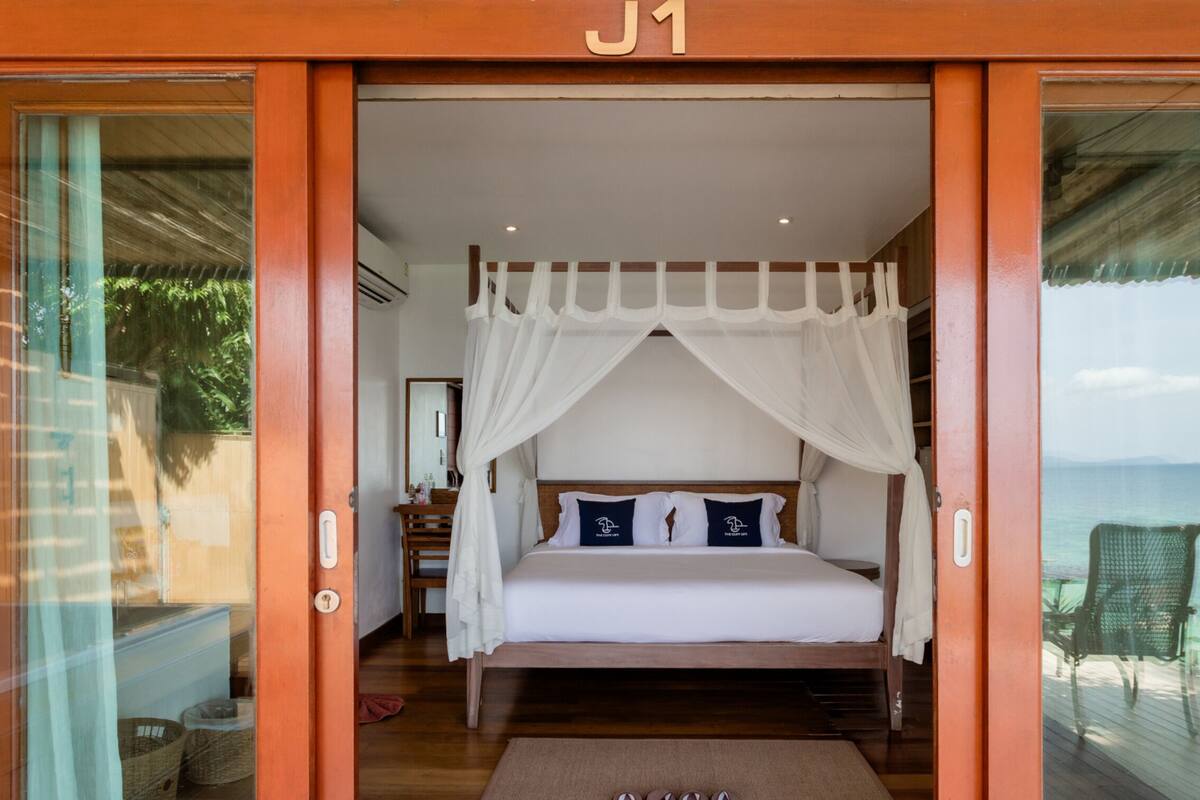 Un dormitorio con cama, cortinas blancas y vista a la playa.
