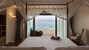 A bedroom with a large bed, a wooden floor, a nightstand, a chair, and a view of the sea through sheer curtains. - The Cliff Lipe (Koh Lipe)