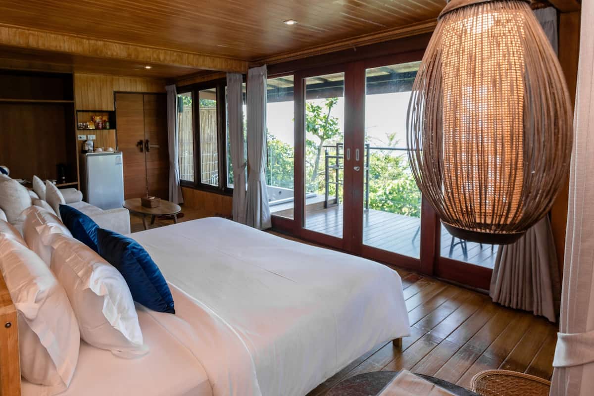 Un dormitorio con una cama grande, suelo de madera, un armario, un escritorio y vistas al exterior.