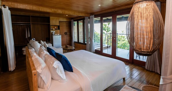 A bedroom with a large bed, wooden flooring, a wardrobe, a desk, and a view of the outdoors.