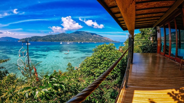 A wooden deck overlooking a clear blue sea with boats and a distant island. - The Cliff Lipe (Koh Lipe)