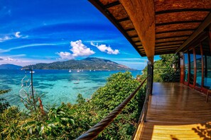 A wooden deck overlooking a clear blue sea with boats and a distant island.