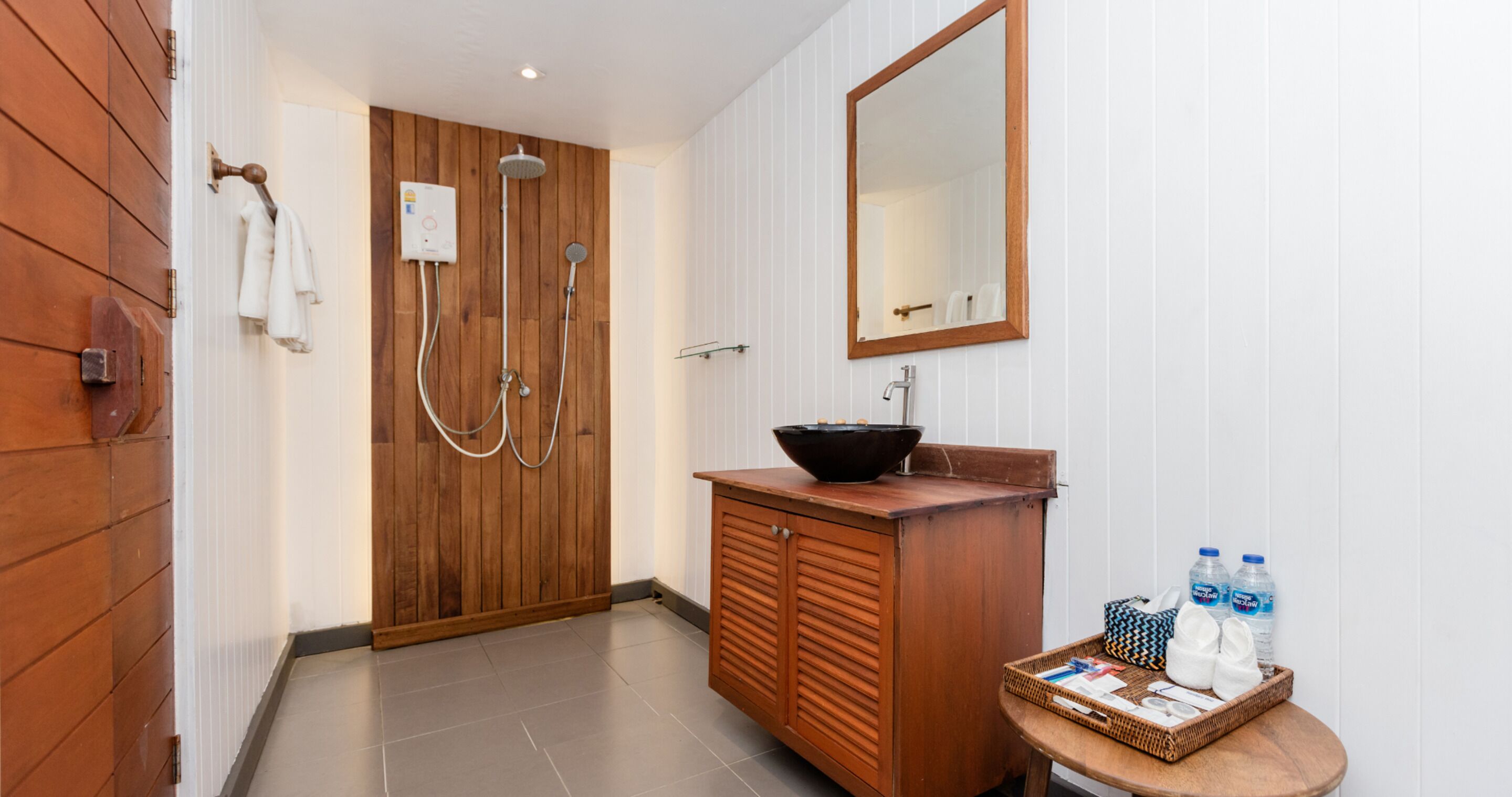 A bathroom with a wooden door, a sink with a black basin, a mirror, and a small table with toiletries.