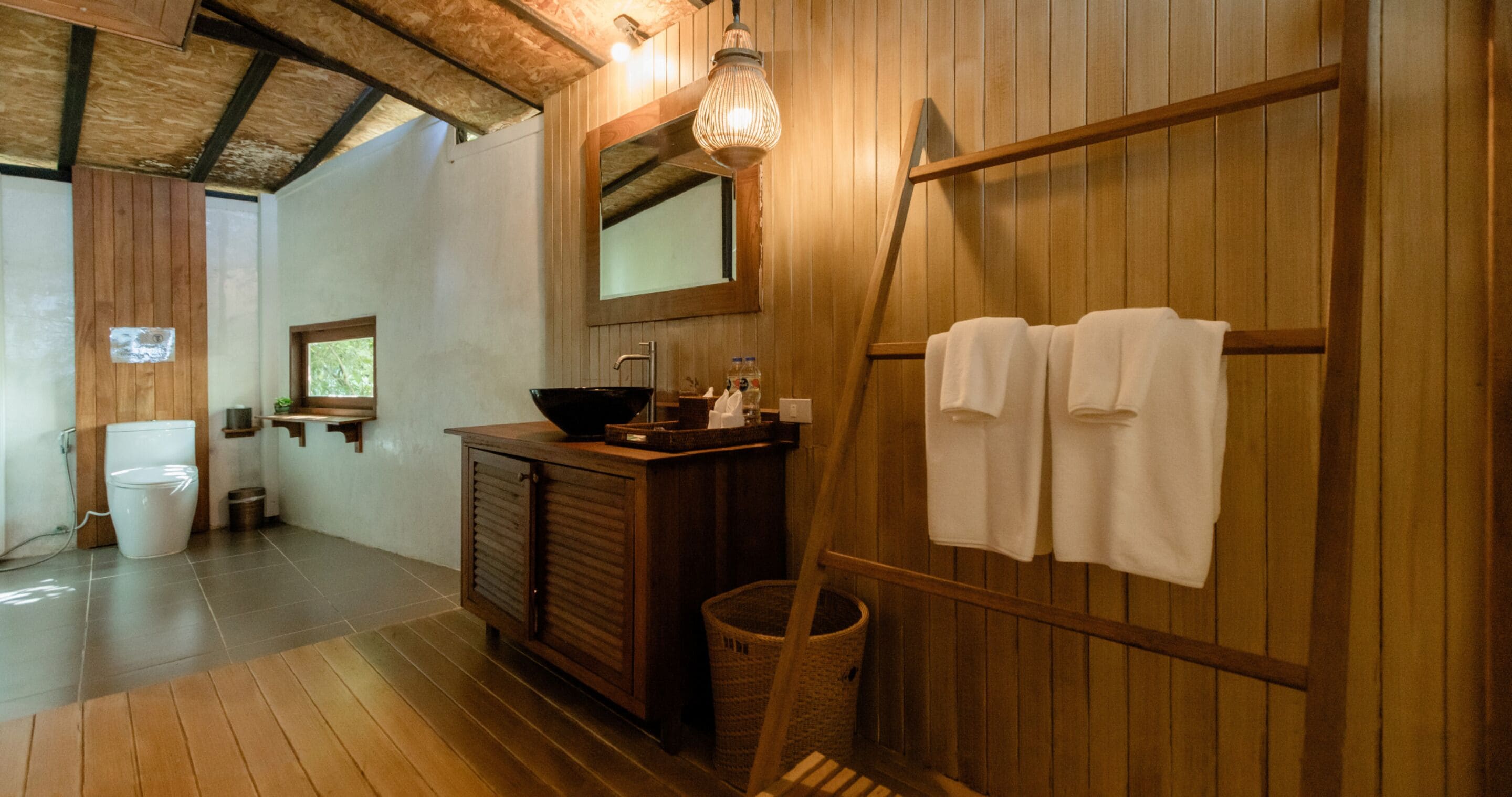 A wooden bathroom with a sink, mirror, and towels on a rack.