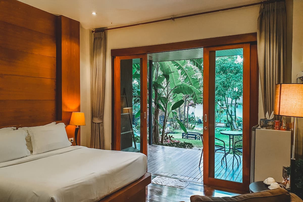 Habitación de hotel con cama, mesita de noche, lámpara, escritorio y vistas a un jardín por una puerta de cristal.