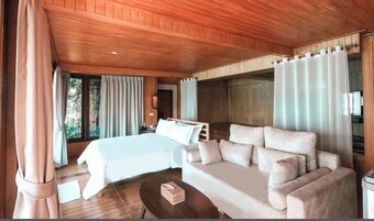 Un dormitorio con cama, sofá, una mesita y ventana con cortinas.