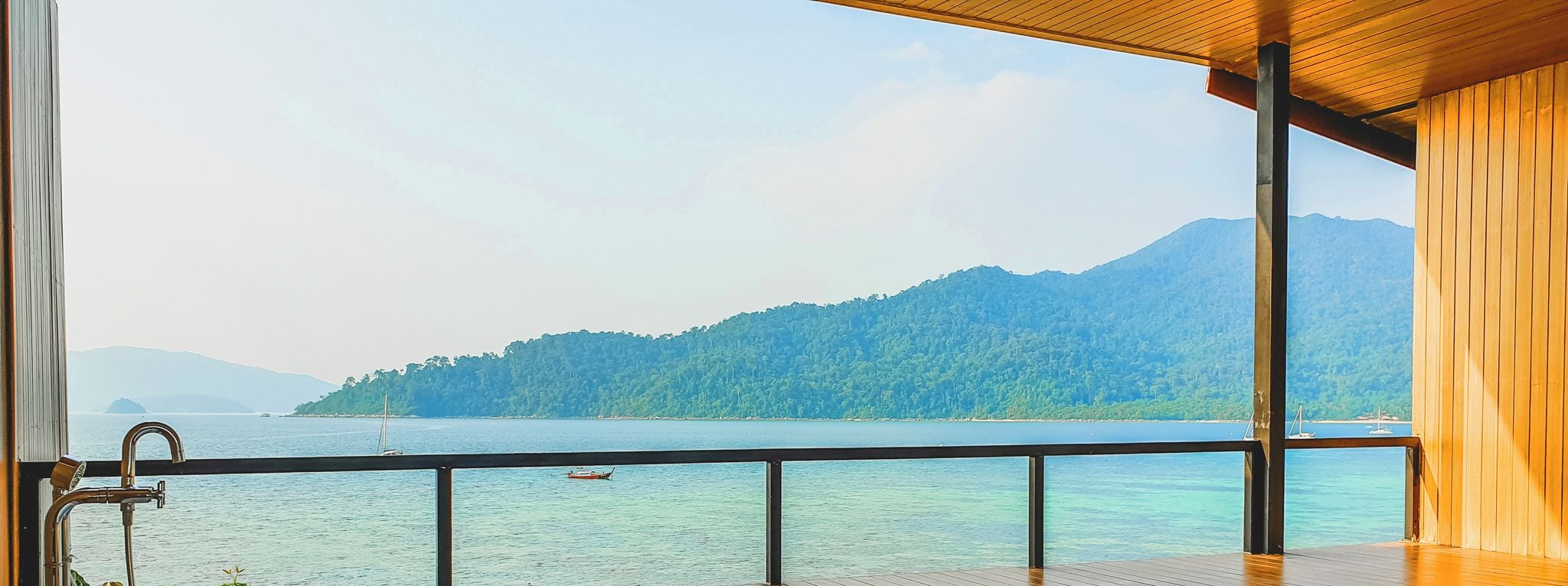 A wooden deck with a large bathtub and a view of a calm lake and distant mountains.