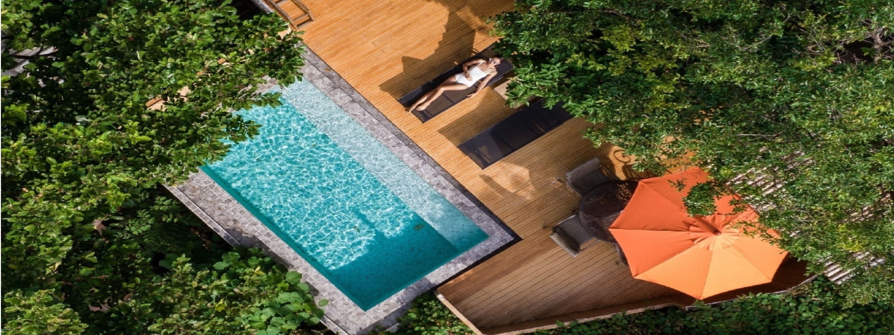 Vista aérea de una piscina rectangular con cubierta de madera y sillas de descanso.