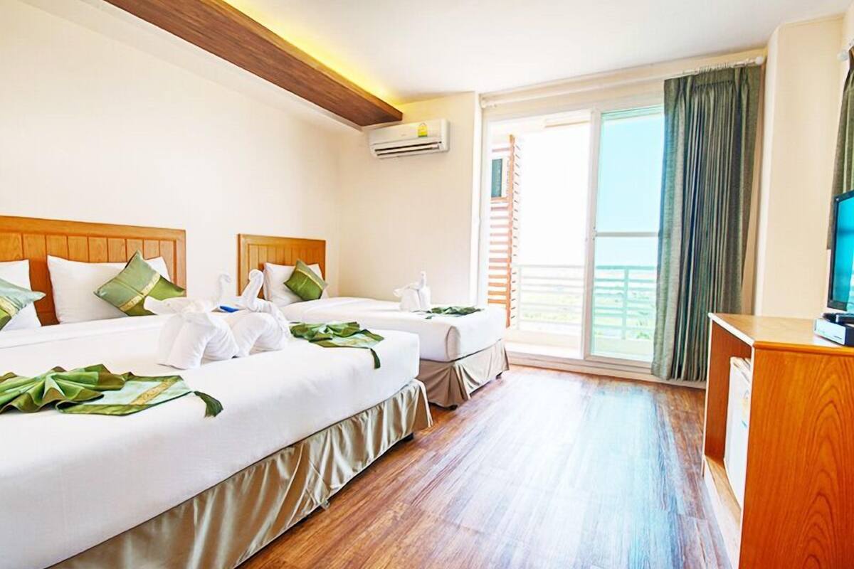 A hotel room with two beds, a wooden ceiling, an air conditioning unit, a TV, and a balcony with curtains.