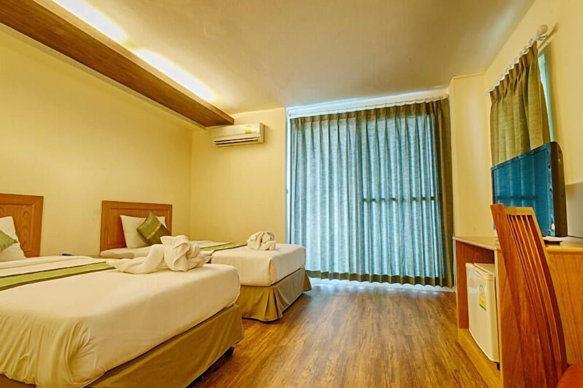 A hotel room with two beds, a desk, a chair, an air conditioning unit, and a window with curtains.