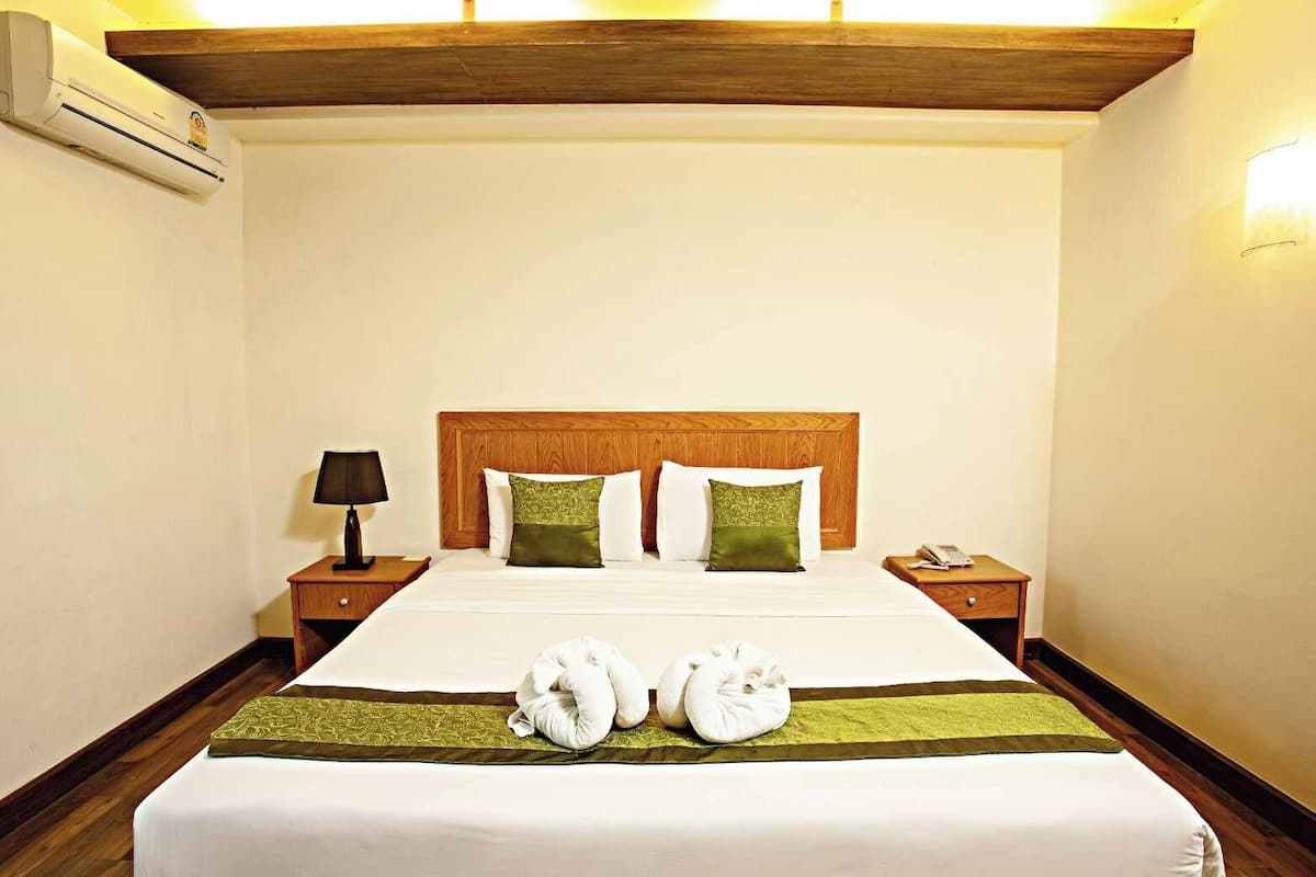 A hotel room with a wooden headboard, a bed with white and green pillows, a bedside table with a lamp, and a bedside phone.