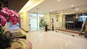 A modern hotel lobby with a glass entrance, a reception desk, and a seating area with a floral arrangement. - TM Land Hotel (Bang Pa-in)