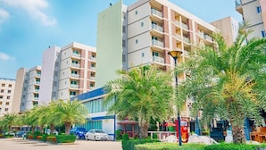 A multi-story residential building with balconies, surrounded by palm trees and a street with parked cars. - TM Land Hotel (Bang Pa-in)