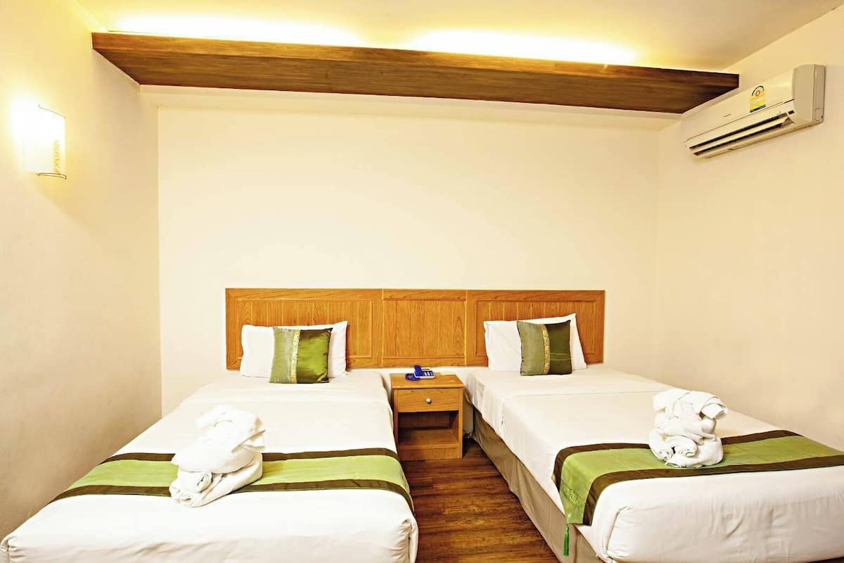 A hotel room with two beds, wooden headboards, a nightstand, a wall-mounted air conditioner, and a bedside lamp.