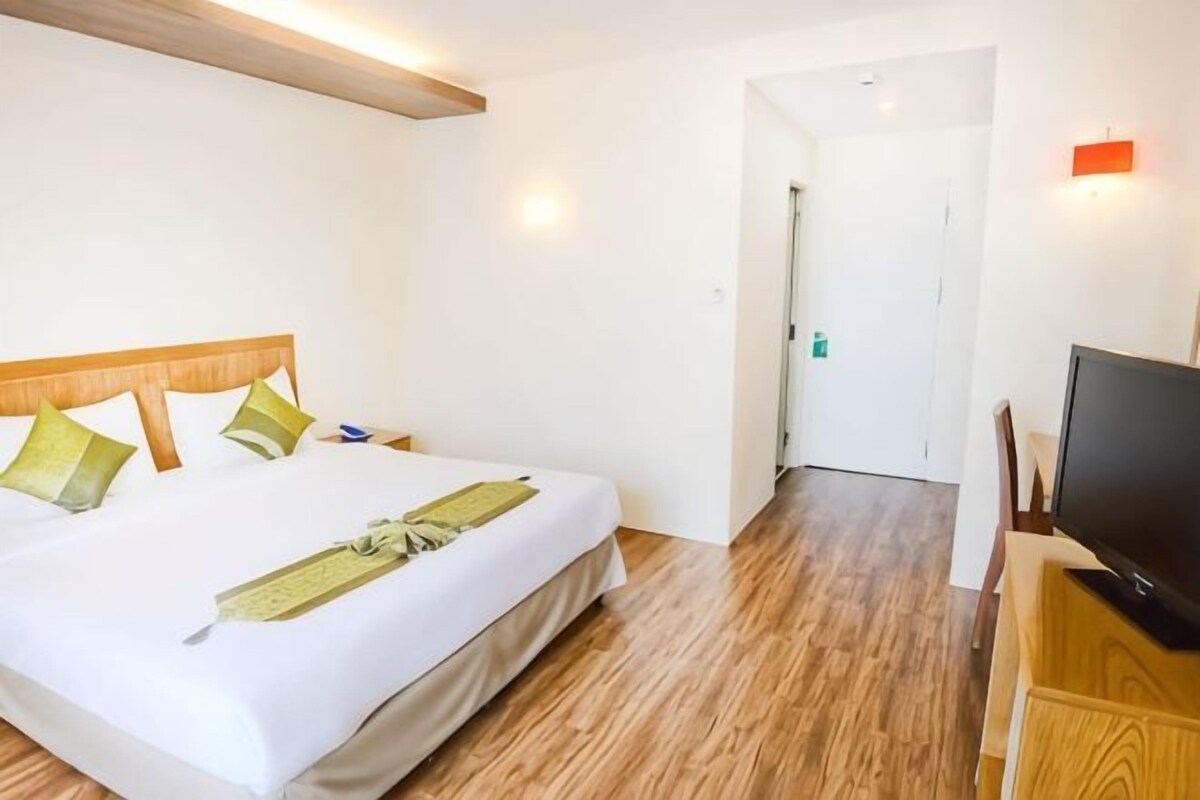 A hotel room with a bed, wooden flooring, a television, and a door leading to another room.