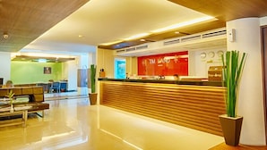 A modern hotel lobby with a reception desk, seating area, and a green wall in the background. - TM Land Hotel (Bang Pa-in)