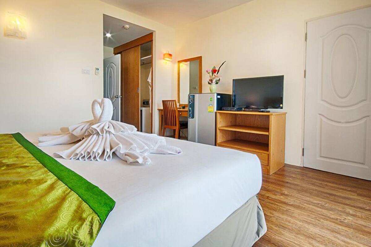 A hotel room with a neatly made bed, a desk with a computer, a television, and a door.