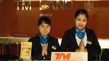 Two receptionists at a TM LAND serviced hotel reception desk with a sign indicating it is for reception and cashier.