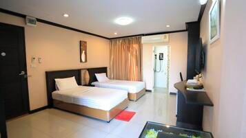 A hotel room with two beds, a TV, a desk, and a bathroom visible through a door.