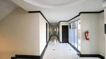 A hallway with a fire extinguisher mounted on the wall, a door at the end, and a window on the right side.