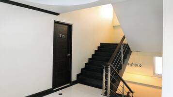Un interior limpio y moderno con una escalera negra, suelo de baldosas blancas y una puerta con la etiqueta 'T35'.