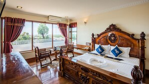 Una habitación de hotel con una cama grande, muebles de madera, un escritorio y ventanas amplias con cortinas.