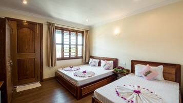 Habitación de hotel con dos camas, piso de madera, un ventanal grande con cortinas y un armario de madera.